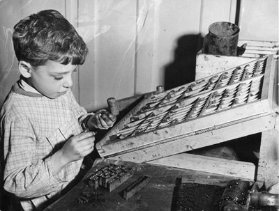 Enfant de sept ans composant un texte devant une casse de caractères d'imprimerie